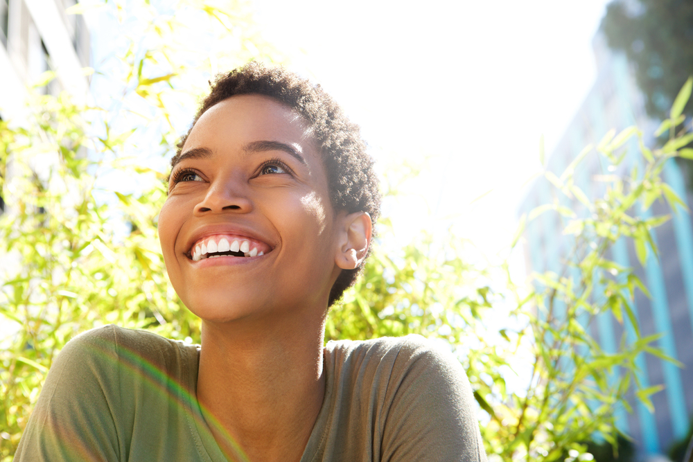 A younger woman smiling and looking up with plants behind her