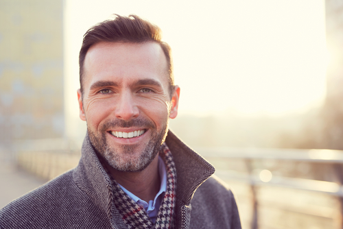 A middle aged man smiling with sun shining behind her