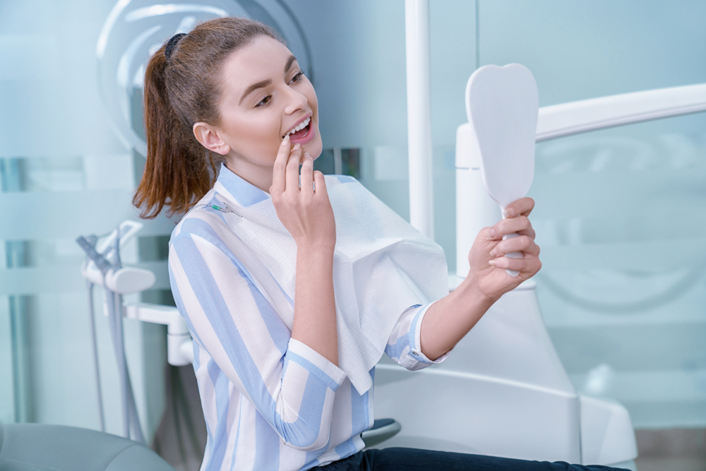 A young woman holding a mirror and looking at her teeth